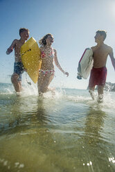 Drei Teenager mit Surfbrettern laufen am Ufer des Meeres - UUF001689