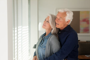 Porträt eines liebenden älteren Paares, das zusammen steht und aus dem Fenster schaut - CHAF000158