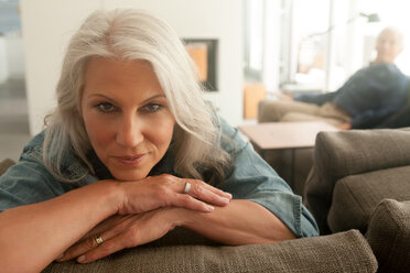 Portrait of happy mature woman sitting on couch with her husband in background - CHAF000165