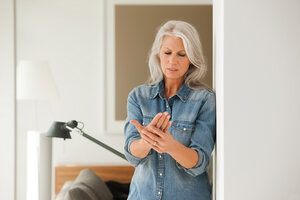 Ältere Frau mit Handschmerzen im Wohnzimmer stehend - CHAF000167