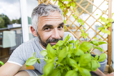 Porträt eines lächelnden Mannes bei der Gartenarbeit auf seinem Balkon - MBEF001107