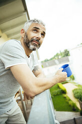 Portrait of man relaxing with cup of coffee on his balcony - MBEF001115