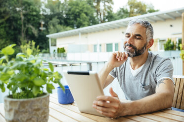 Porträt eines Mannes, der auf seinem Balkon sitzt und ein digitales Tablet benutzt - MBEF001226