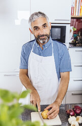 Portrait of man cutting potato in his kitchen - MBEF001123