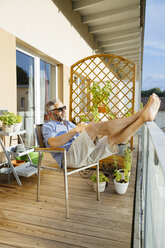 Mann mit Sonnenbrille entspannt auf seinem Balkon - MBEF001130