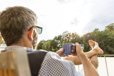 Mann mit einer Tasse Kaffee auf seinem Balkon - MBEF001131