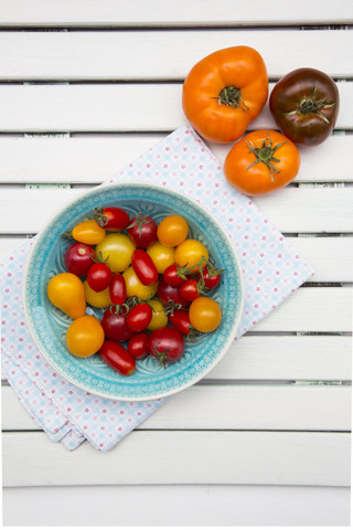Schale mit verschiedenen Heirloom-Tomaten auf Stoff und weißem Holz, lizenzfreies Stockfoto