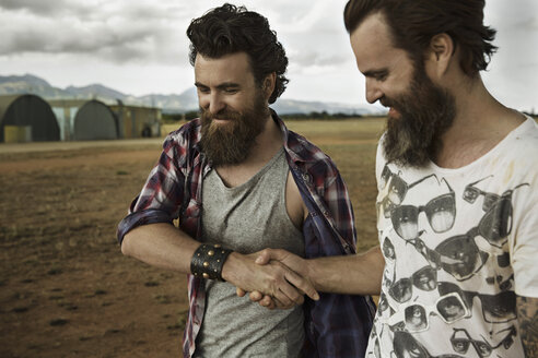 Two men with full beards in abandoned landscape shaking hands - KOF000015