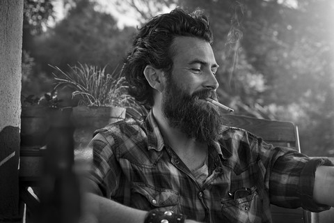 Man with full beard smoking cigarette on porch stock photo