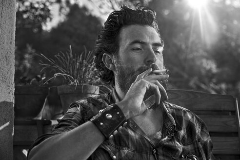 Man with full beard smoking cigarette on porch - KOF000023