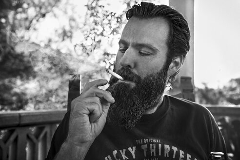 Man with full beard smoking cigarette on porch - KOF000024