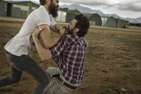 Two men with full beards fighting in abandoned landscape - KOF000042