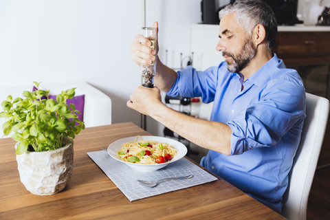 Mann, der seine Nudeln mit Pfeffer würzt, lizenzfreies Stockfoto