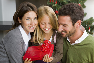 Glückliches Paar und ihre Tochter mit Weihnachtsgeschenk zu Hause - CHAF000190