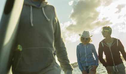 Drei Jugendliche gehen in der Abenddämmerung am Strand spazieren - UUF001702