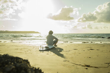 Teenage boy sitting on the beach watching sunset - UUF001703