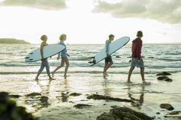 Woman and three teenagers with surfboards walking at waterside of the sea - UUF001708