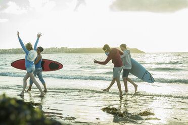 Woman and three teenagers with surfboards running at waterside of the sea - UUF001753