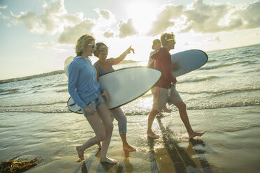 Woman and three teenagers with surfboards walking at waterside of the sea - UUF001712