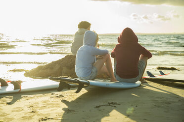 Drei Teenager sitzen am Strand und beobachten den Sonnenuntergang - UUF001718