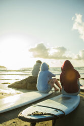 Drei Teenager sitzen am Strand und beobachten den Sonnenuntergang - UUF001719