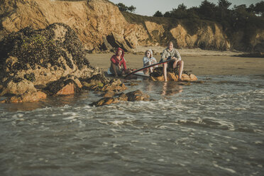 Three teenagers sitting on the beach watching sunset - UUF001720