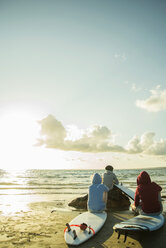 Drei Teenager sitzen am Strand und beobachten den Sonnenuntergang - UUF001721