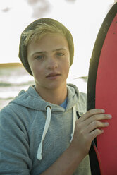 Porträt eines Teenagers, der mit seinem Surfbrett am Strand steht - UUF001730
