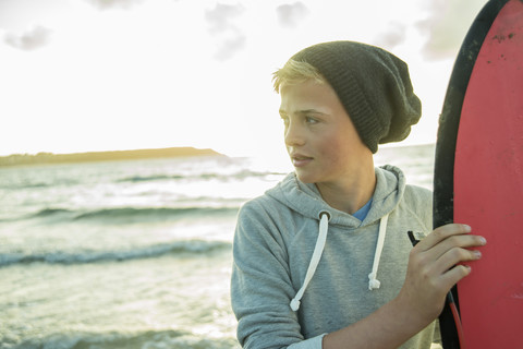 Porträt eines Teenagers, der mit seinem Surfbrett am Strand steht, lizenzfreies Stockfoto