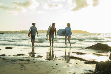 Three teenagers with surfboards walking on the beach at evening twilight - UUF001732