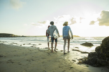 Three teenagers with surfboards walking on the beach at evening twilight - UUF001733