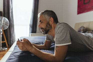 Man lying on his bed using his smartphone - MBEF001180