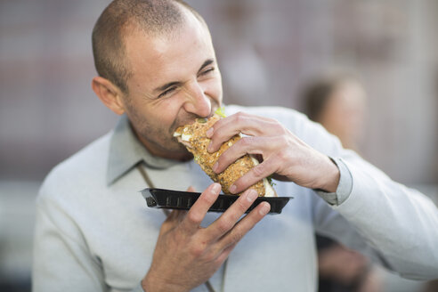 Portrait of businessman eating a sandwich at lunchtime - ZEF000258