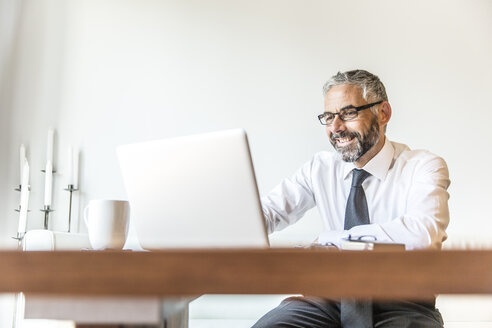 Portrait of smiling businessman working at home office - MBEF001233