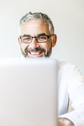 Porträt eines lachenden Geschäftsmannes, der am Laptop arbeitet - MBEF001165