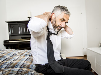 Businessman binding tie in his bedroom - MBEF001219