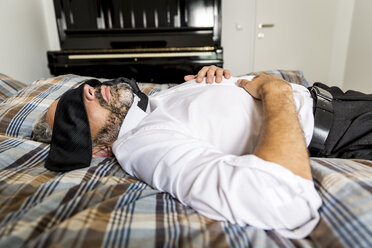 Businessman lying on his bed with tie covering his eyes - MBEF001220