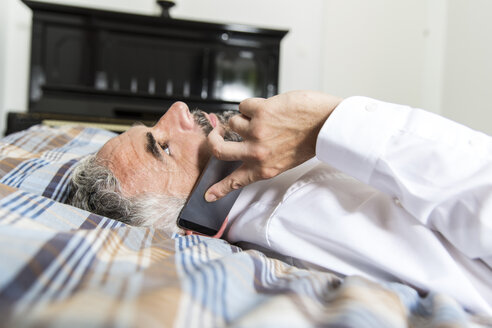 Geschäftsmann liegt auf seinem Bett und telefoniert mit seinem Smartphone - MBEF001222