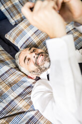 Portrait of happy businessman lying on his bed looking at his smartphone - MBEF001177