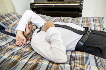 Businessman relaxing on his bed covering eyes with his arm - MBEF001223