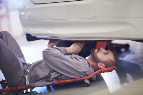 Automechaniker auf einem Kriechwagen bei der Arbeit in einer Reparaturwerkstatt - ZEF000541