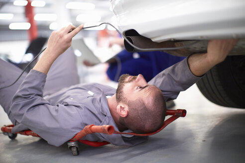 Automechaniker auf einem Kriechwagen bei der Arbeit in einer Reparaturwerkstatt - ZEF000515