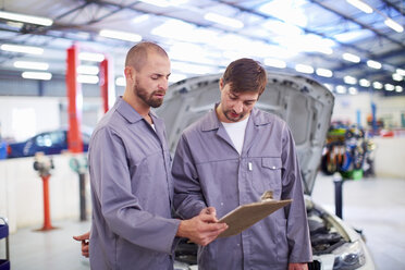 Zwei Automechaniker mit Klemmbrettern in einer Reparaturwerkstatt - ZEF000523