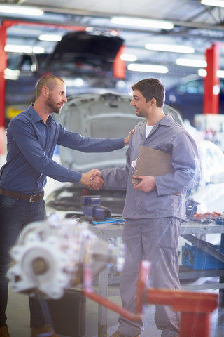 Car mechanic and client shaking hands in repair garage stock photo