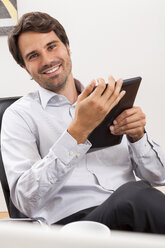 Smiling young businessman with tablet computer in his office - JUNF000041