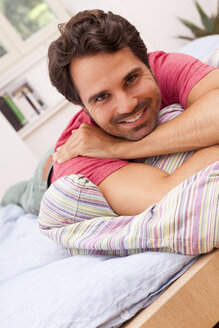 Porträt eines lächelnden jungen Mannes, der auf seinem Bett liegt - JUNF000049