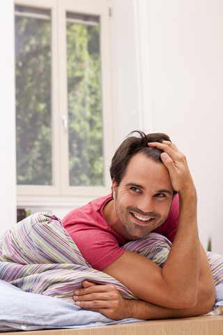 Porträt eines lächelnden jungen Mannes, der auf seinem Bett liegt, lizenzfreies Stockfoto