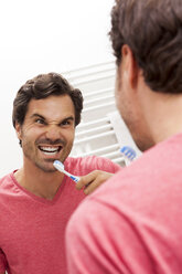 Spiegelbild eines Mannes mit Zahnbürste, der den Mund aufreißt - JUNF000054