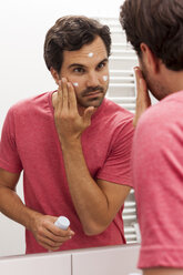 Mirror image of young man applying face cream - JUNF000055