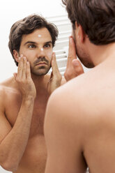 Mirror image of young man applying face cream - JUNF000057